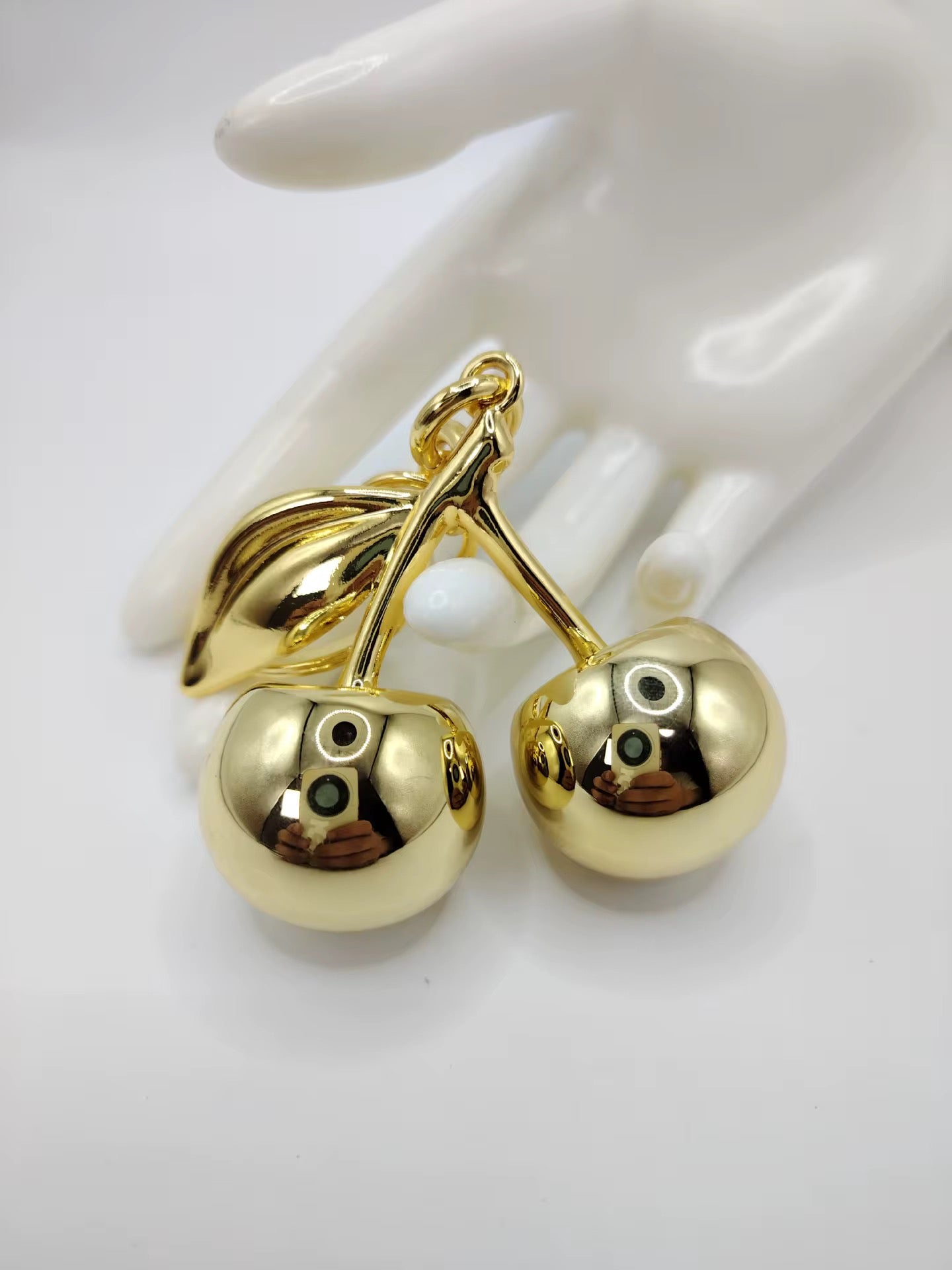 Gold cherry-shaped pendant on a white mannequin hand